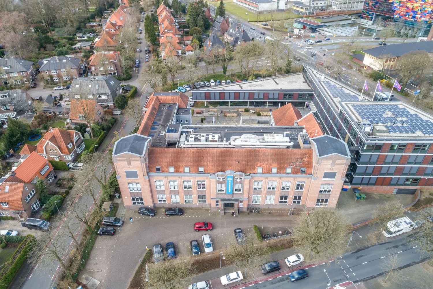 Luchtfoto van het gebouw aan de Lage Naarderweg in Hilversum, omringd door woonhuizen en wegen.
